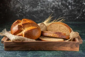 Whole and cut fresh bread in a brown wooden box on dark background