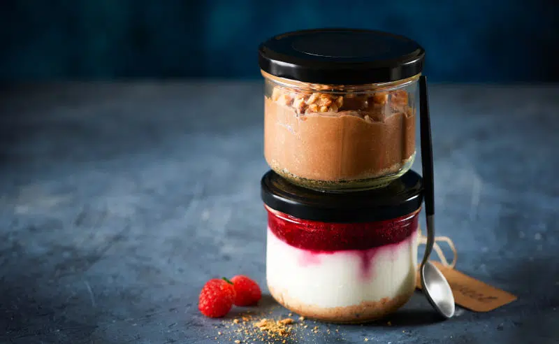 Two homemade easy cheesecakes in jars with chocolate mousse and raspberry curd sauce on a dark blue background