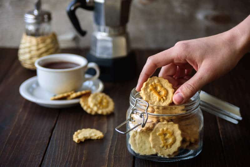 Jar with bitcoin symbol cookies and coffee on wooden board