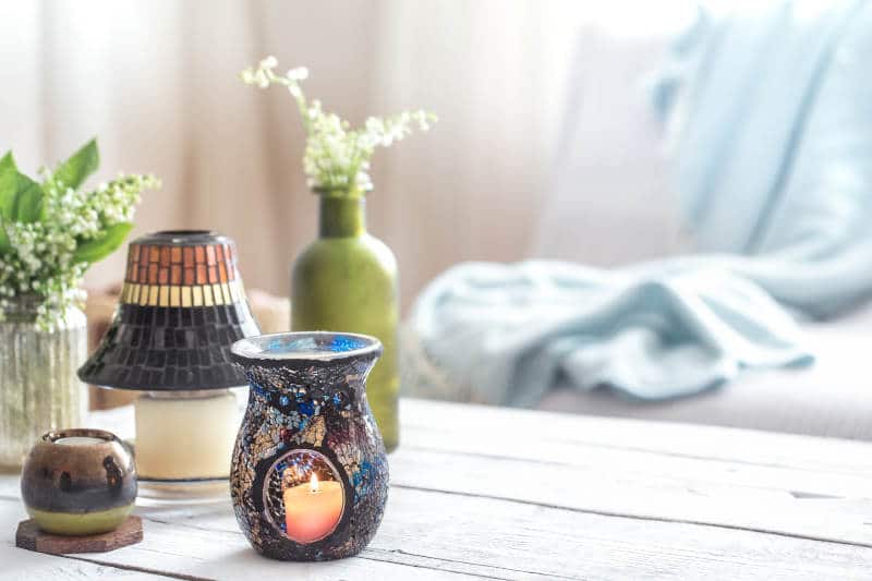 Beautiful burning candles with green leaves in purse on white wooden table