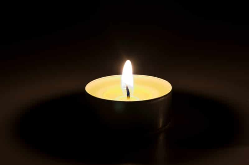 One yellow burning candle in the dark