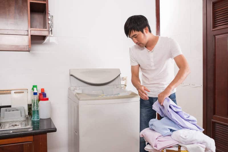 Young man putting dirty clothes in washing machine