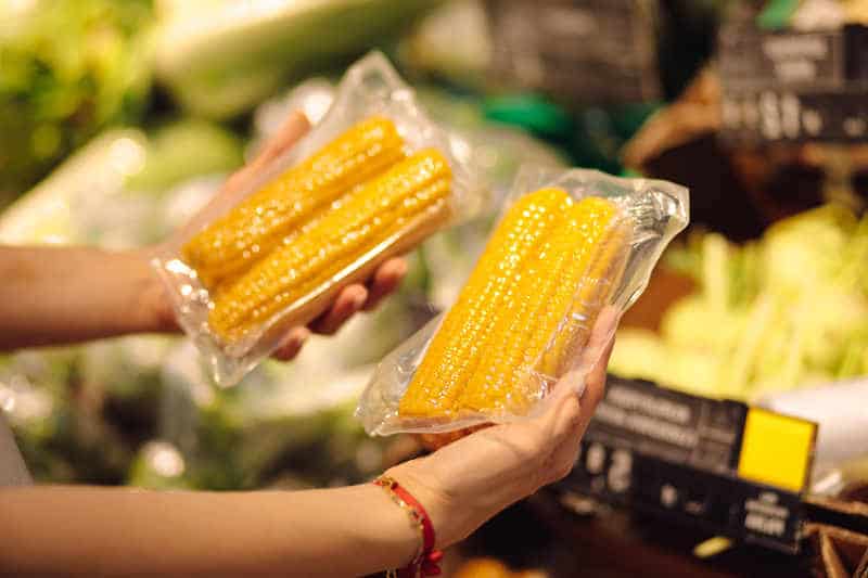 Young man is holding two bags of sweet corn in vacuum package