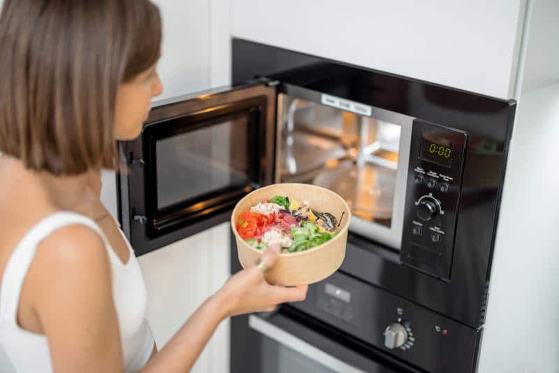 Woman heating food with microwave machine at dorm