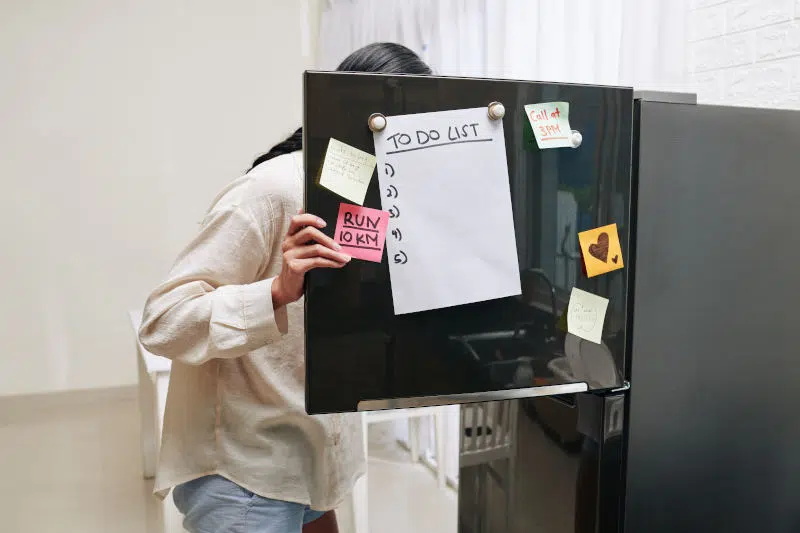 Young woman opening fridge door covered with motivating stickers