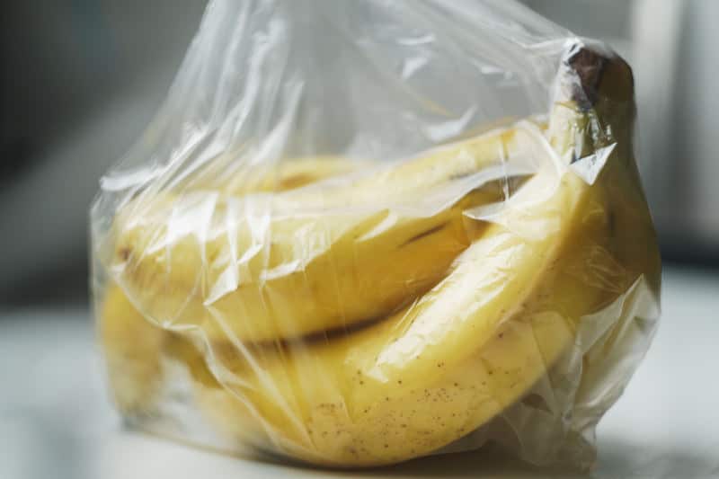 A bunch of almost ripe bananas wrapped in a transparent plastic bag