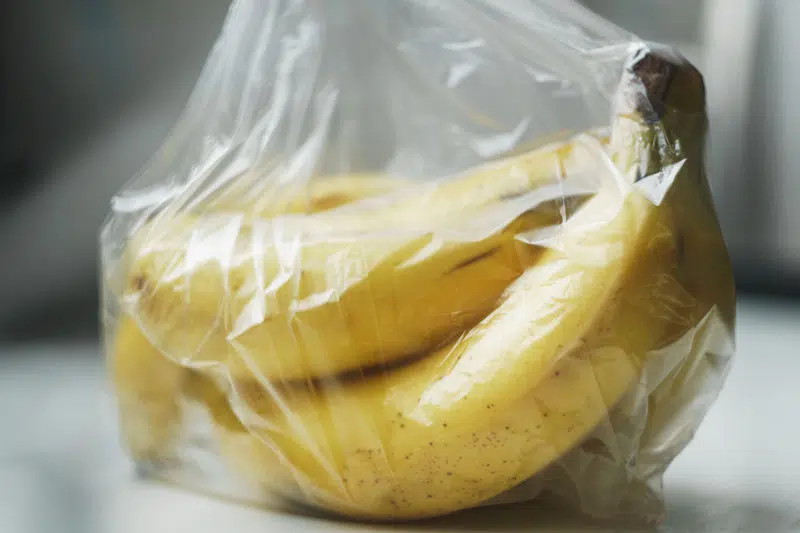 A bunch of almost ripe bananas wrapped in a transparent plastic bag