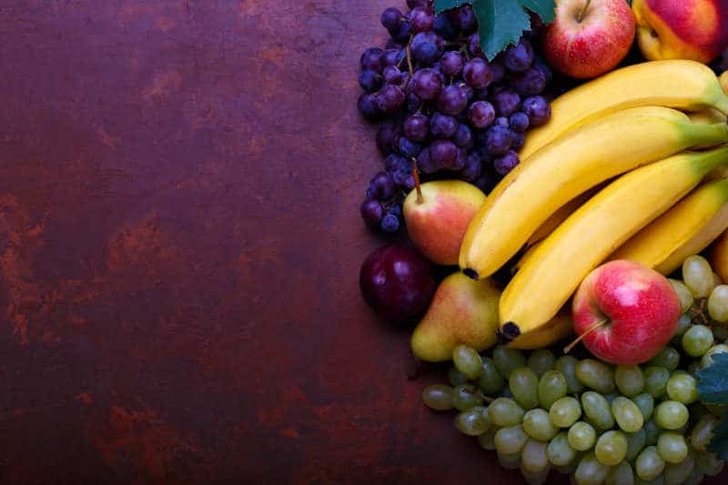 Bananas, pear, plum, peach, apples, red and white grapes on rustic background.