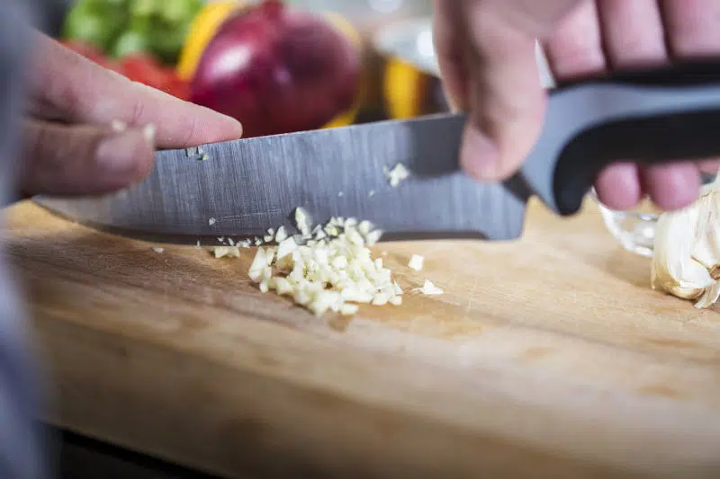 Chef chopping fresh garlic with knife on a board