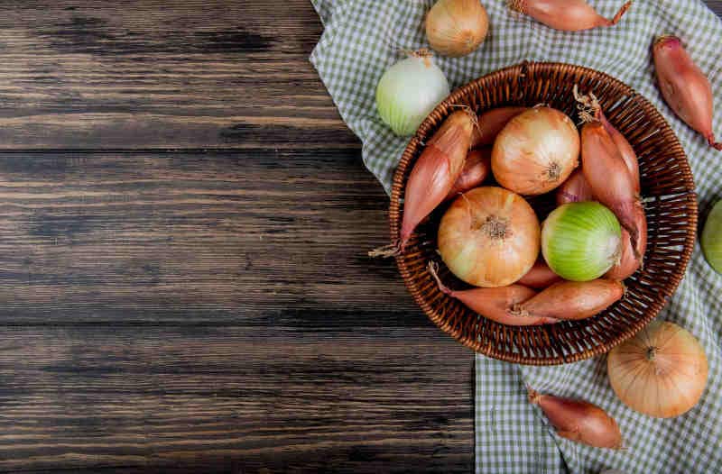 Top view of onions as shallot sweet and white ones in basket on plaid cloth and wooden background