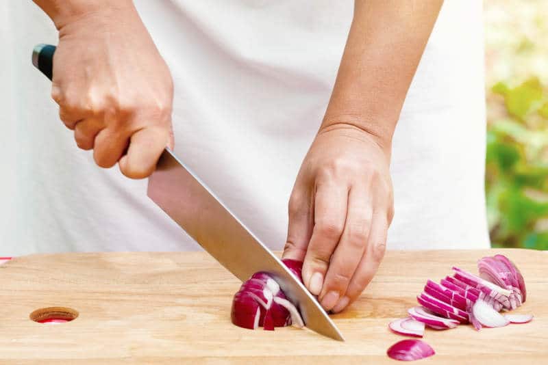 Female hands cut onions on a wooden board