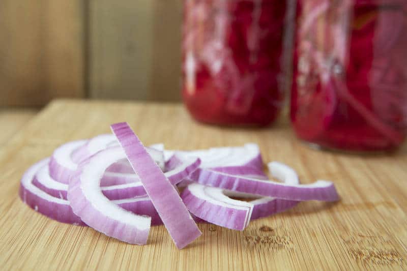 Red onion slices on cutting board with jars for pickling.