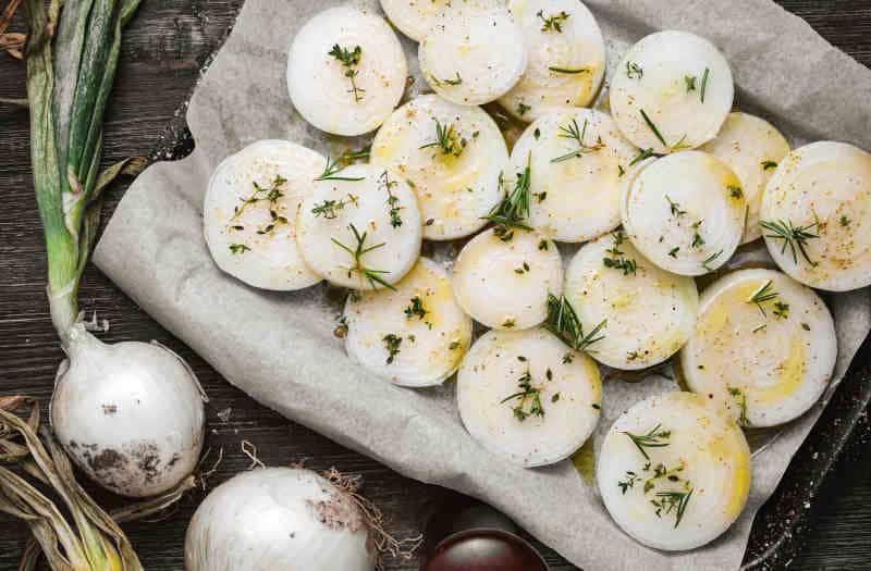 Raw onion slices with olive oil and herbs on a baking sheet, ready for roasting.