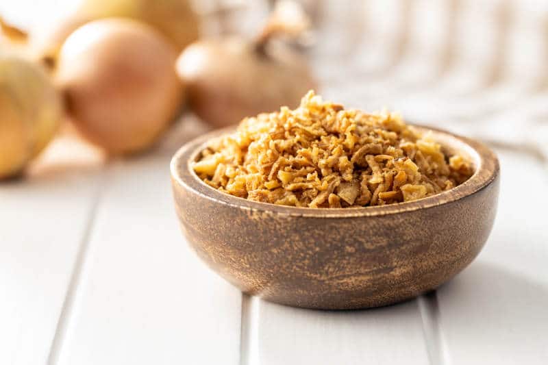 Pieces of fried onions in bowl on white table.