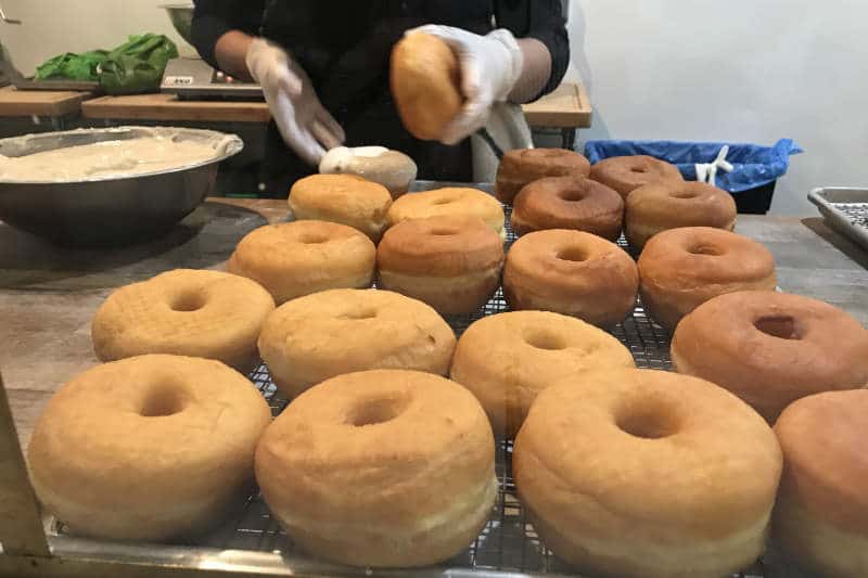 A cook is glazing donuts for sale at a donut shop