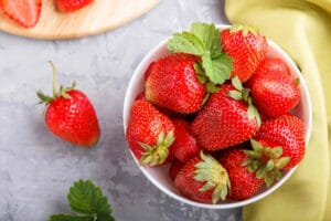 Fresh red strawberry in white bowl on gray concrete background.