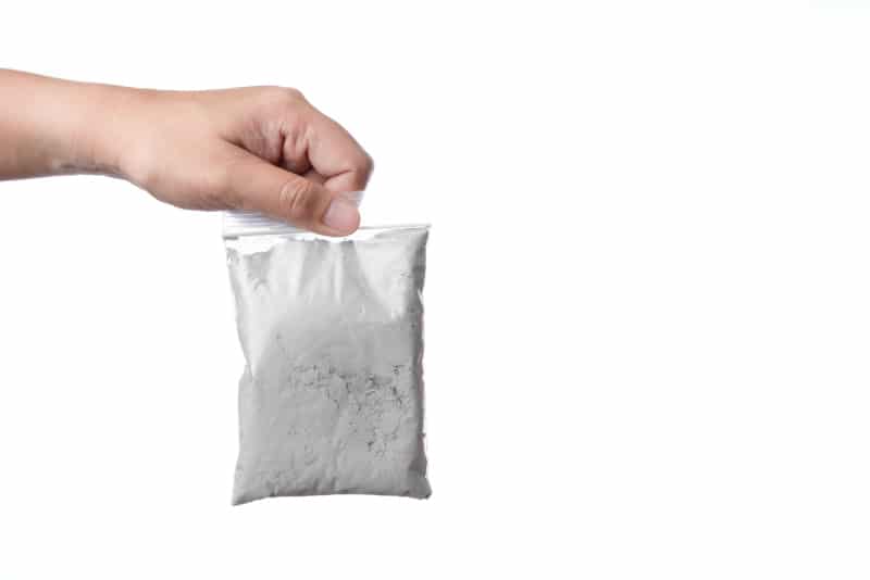 Hand holding plastic zipper bag of burned charcoal ash powder on white background