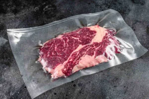 Raw rib eye beef meat steak in vacuum packaging. Black background. Top view.