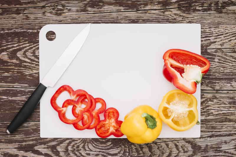 Sices of peppers with knife on white plastic cutting board