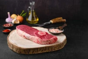 Raw chuck eye steak, onions and olive oil on kitchen table ready for cooking