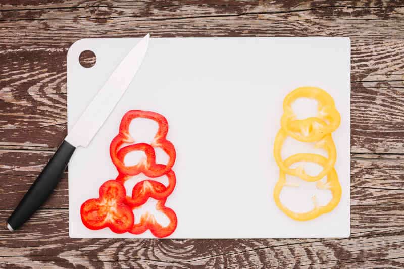 Slices of red-yellow bell pepper and knife on plastic cutting board