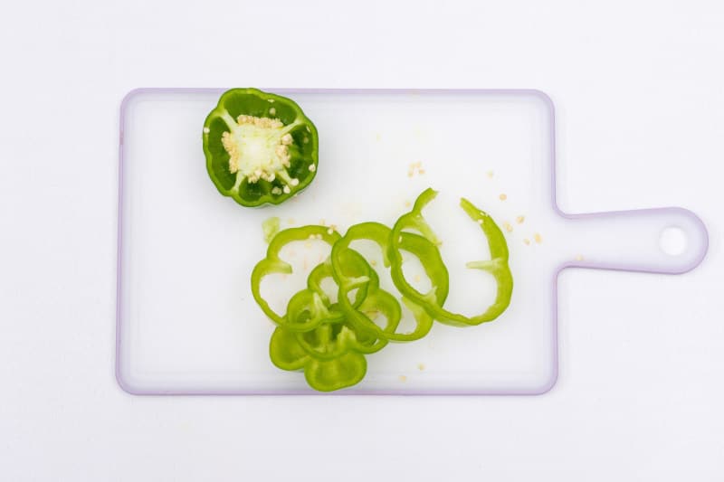 Green bell pepper sliced on plastic cutting board on white background