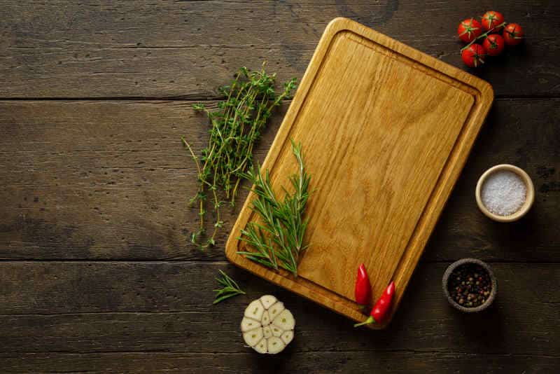 Spices, herbs and wood cutting board on dark wooden backdrop.
