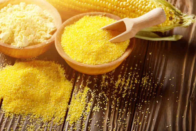 Bowl of corn grits corncob and corn flour on kitchen table