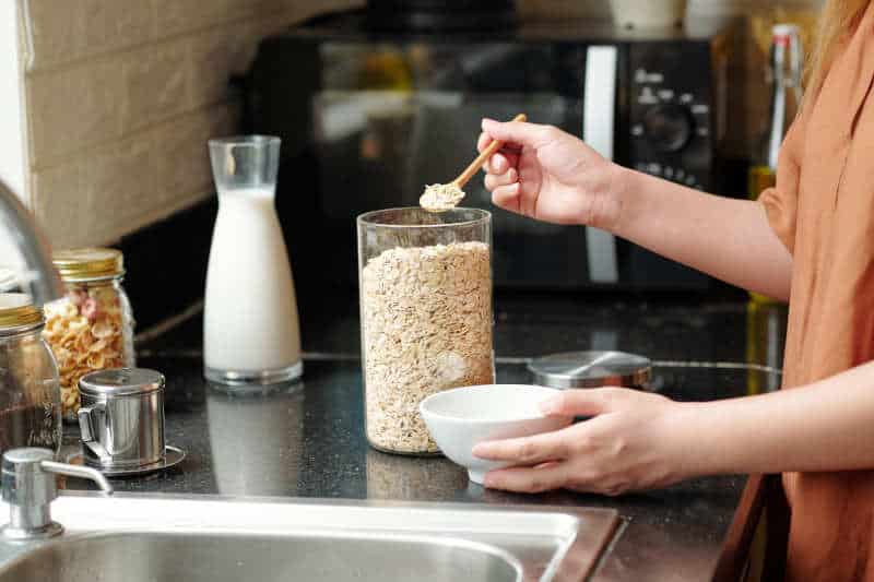 Woman standing at kitchen counter and putting instant oatmeal in bowl