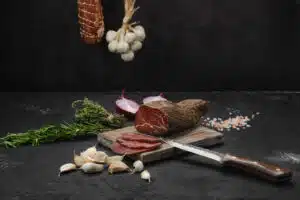 Beef jerky, knife and garlic on bamboo cutting board