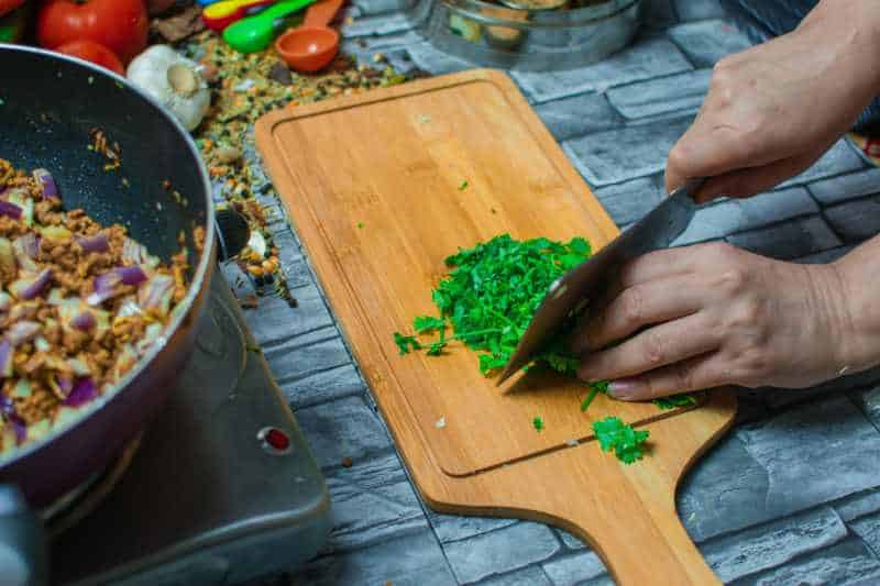 Woman cutting coriander leaves on wood cutting boards while preparing the food