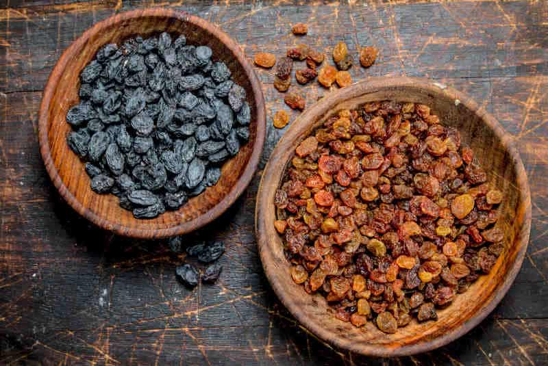 The raisins in the bowls on a wooden background.