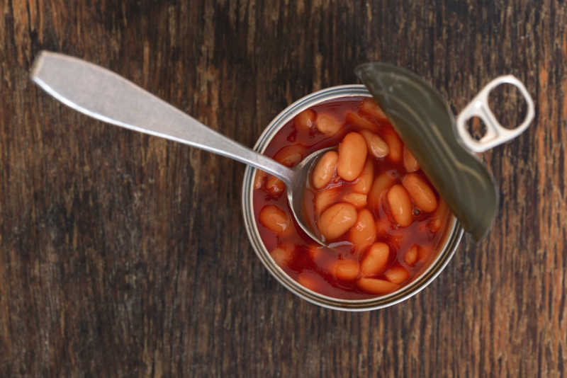 Canned beans in a tin with spoon on wooden background