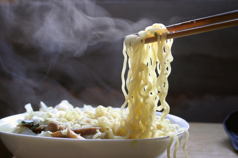 Chopsticks picking up rice noodles from a steaming hot bowl.